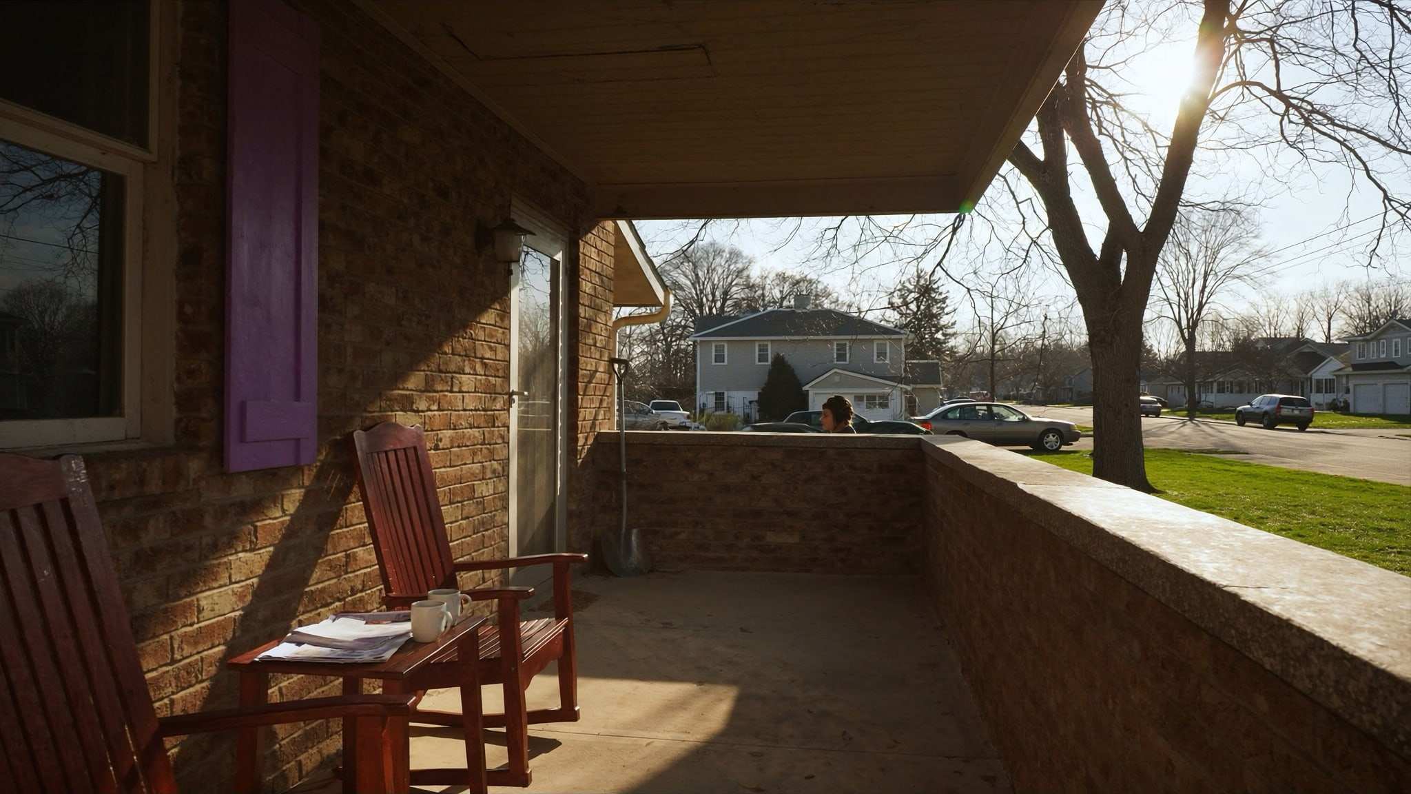 Front porch of a brick home with two chairs, coffee mugs and a folder of papers