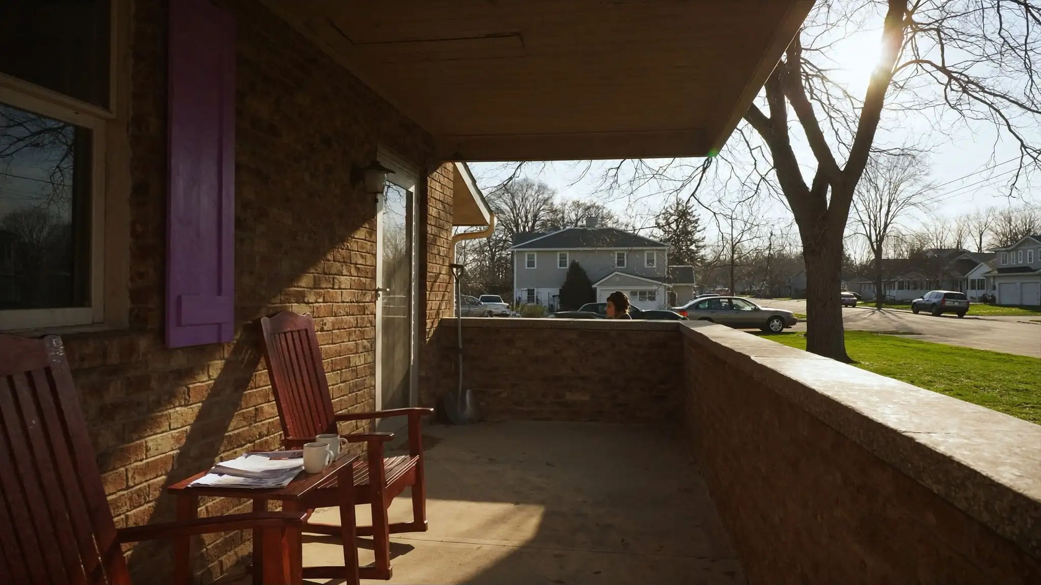 Front porch of a brick home with two chairs, coffee mugs and a folder of papers
