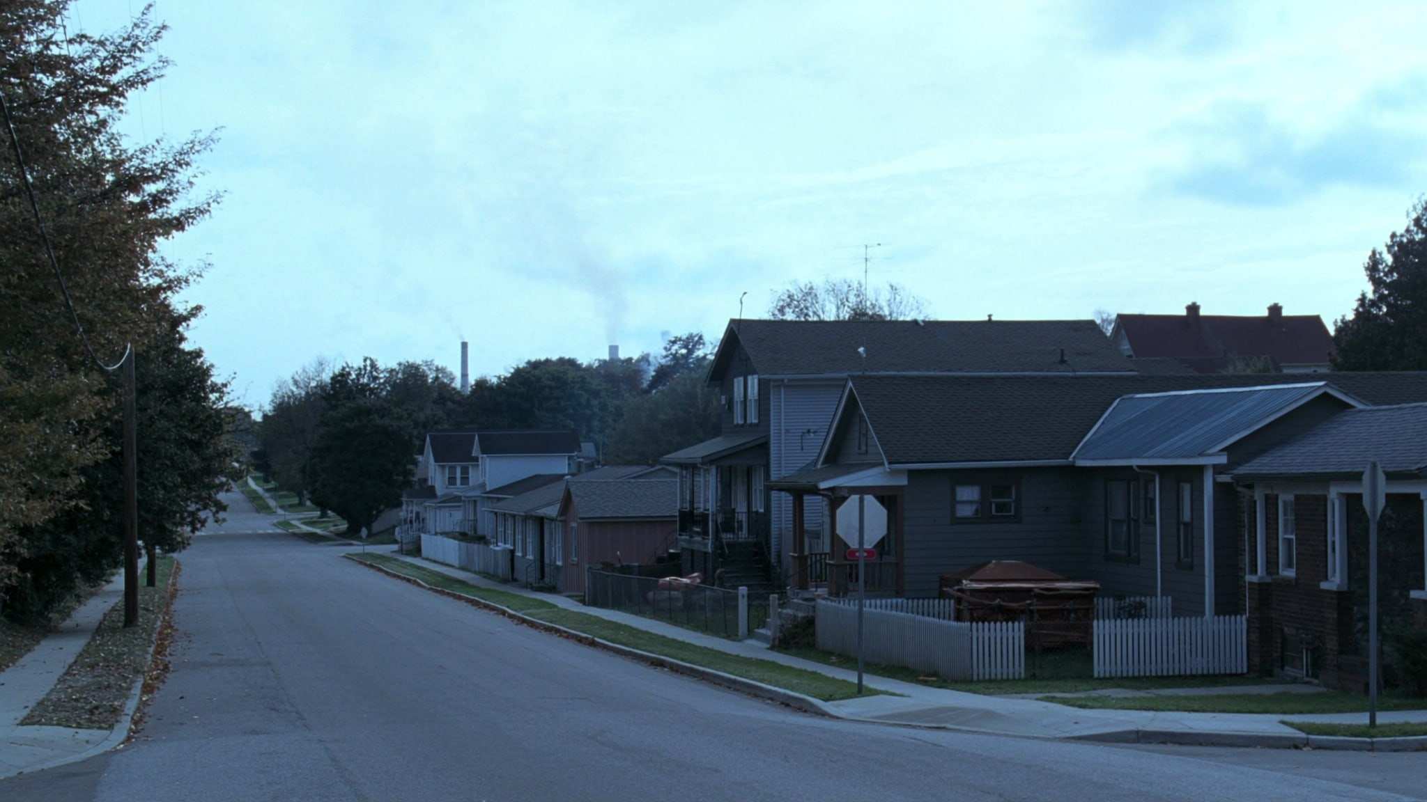 Modest older homes on a residential street, with mill stacks on the horizon