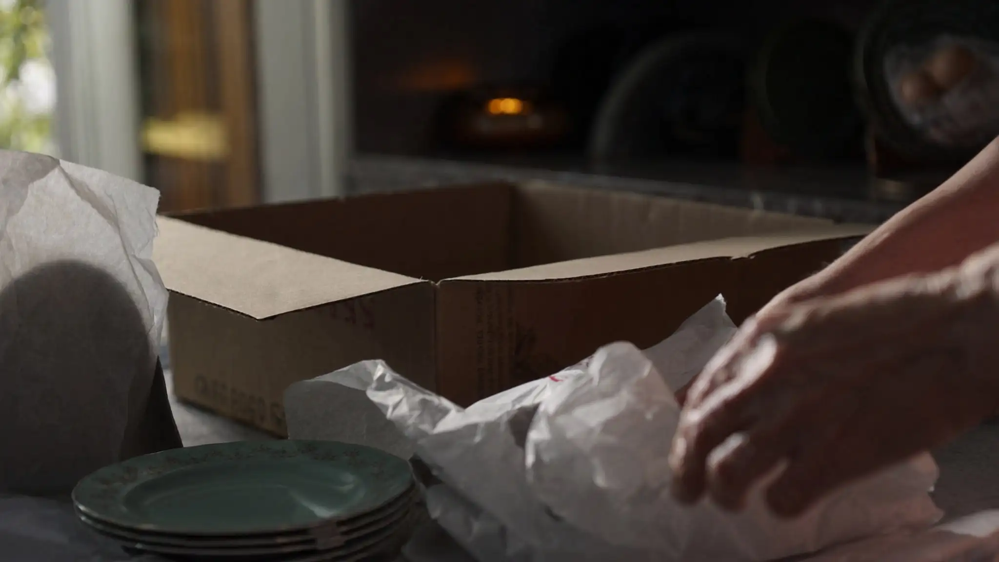 Hands wrapping dishes in packing paper next to a moving box
