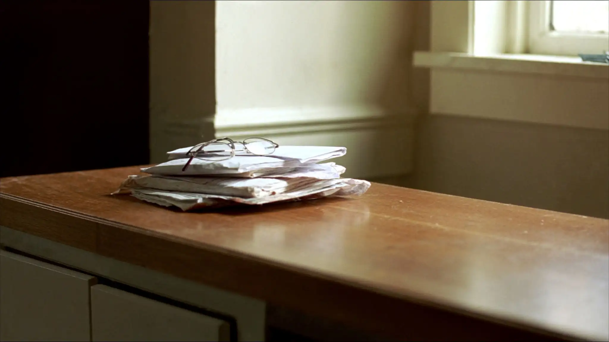 Stack of unopened mail and reading glasses on a kitchen counter